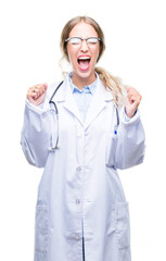 Beautiful young blonde doctor woman wearing medical uniform over isolated background excited for success with arms raised celebrating victory smiling. Winner concept.