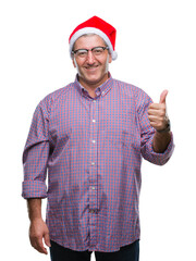 Handsome senior man wearing christmas hat over isolated background doing happy thumbs up gesture with hand. Approving expression looking at the camera with showing success.