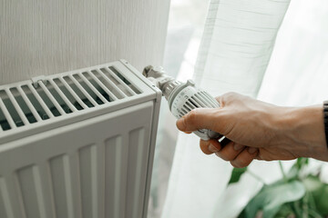 A man regulates the temperature on the radiator at home. Rising prices for heating in households....