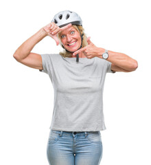 Middle age caucasian cyclist woman wearing safety helmet over isolated background smiling making frame with hands and fingers with happy face. Creativity and photography concept.