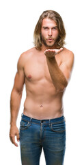 Young handsome shirtless man with long hair showing sexy body over isolated background looking at the camera blowing a kiss with hand on air being lovely and sexy. Love expression.