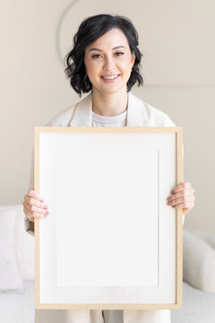 Smiling middle-aged woman holding a framed picture under glass with a blank white sheet. Template for advertising and messages. Business concept.
