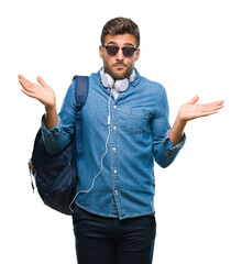 Young handsome tourist man wearing headphones and backpack over isolated background clueless and...