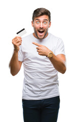 Young handsome man holding credit card over isolated background very happy pointing with hand and...