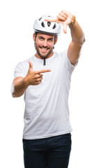 Young handsome man wearing cyclist safety helmet over isolated background smiling making frame with hands and fingers with happy face. Creativity and photography concept.