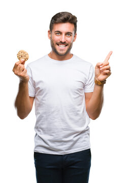 Young handsome man eating chocolate chips cookie over isolated background very happy pointing with hand and finger to the side