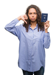 Fototapeta premium Young hispanic woman holding passport of Germany with angry face, negative sign showing dislike with thumbs down, rejection concept