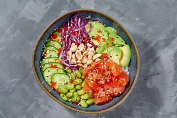 Top view on poke salad with salmon and green vegetable in the bowls on gray background. Copy space.