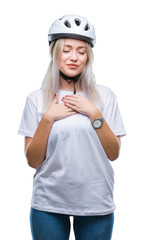 Young blonde woman wearing cyclist security helmet over isolated background smiling with hands on chest with closed eyes and grateful gesture on face. Health concept.