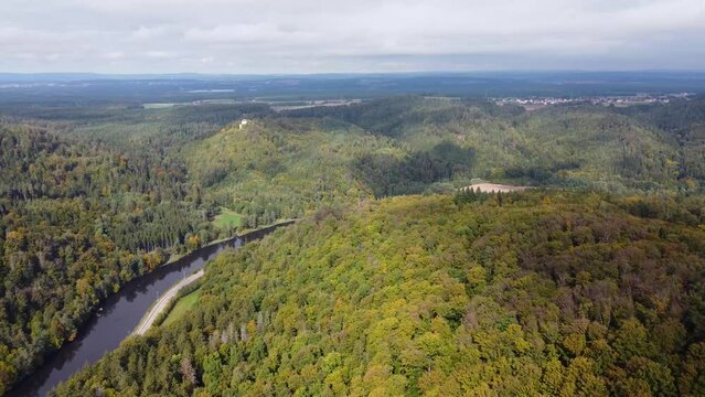 Drone flying over valley of the river Regen in Bavaria with mixed forest in autumn and old castle on hilltop on sunny day