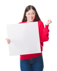 Young Chinese woman over isolated background holding blank banner screaming proud and celebrating victory and success very excited, cheering emotion