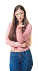 Obraz premium Young Chinese woman over isolated background wearing glasses looking at the camera blowing a kiss with hand on air being lovely and sexy. Love expression.