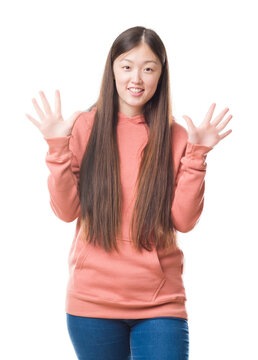 Young Chinese woman over isolated background wearing sport sweathshirt showing and pointing up with fingers number ten while smiling confident and happy.