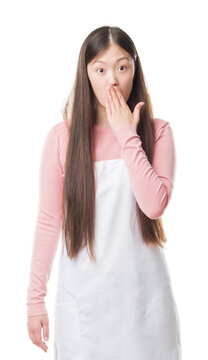 Young Chinese shop owner woman over isolated background wearing white apron cover mouth with hand shocked with shame for mistake, expression of fear, scared in silence, secret concept
