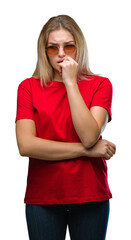 Young caucasian woman wearing sunglasses over isolated background looking stressed and nervous with hands on mouth biting nails. Anxiety problem.