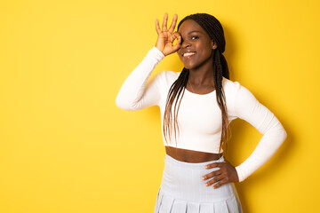 Photo of pretty young african american woman wear white sweater showing okay isolated yellow background