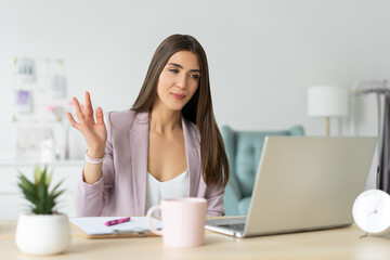 Responsive kind woman psychologist greets her client by video call. Waving hand at the camera laptop beech. Remote reception. - obrazy, fototapety, plakaty