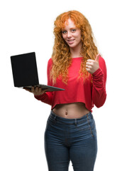 Young redhead woman using computer laptop happy with big smile doing ok sign, thumb up with fingers, excellent sign