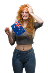 Young redhead woman holding flag of Australia stressed with hand on head, shocked with shame and...