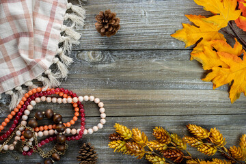 Autumn flatlay concept, with dried flowers, coral pink jewelry beads, plaid towel, and pine cones on a wood background