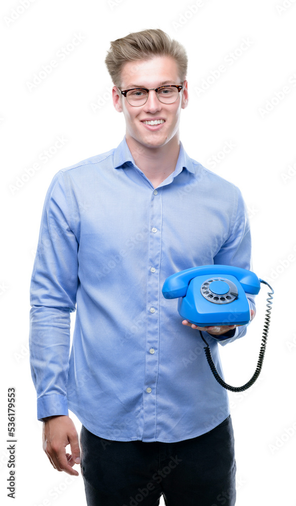 Poster Young handsome blond man holding vintage telephone with a happy face standing and smiling with a confident smile showing teeth