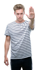 Naklejka premium Young handsome blond man wearing stripes sailor t-shirt with open hand doing stop sign with serious and confident expression, defense gesture
