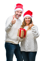 Middle age hispanic couple wearing christmas hat and holding gift over isolated background happy with big smile doing ok sign, thumb up with fingers, excellent sign