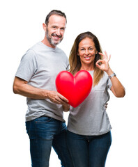 Middle age hispanic casual couple in love holding red heart over isolated background doing ok sign with fingers, excellent symbol