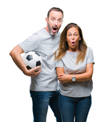 Middle age hispanic couple holding football soccer ball over isolated background scared in shock with a surprise face, afraid and excited with fear expression