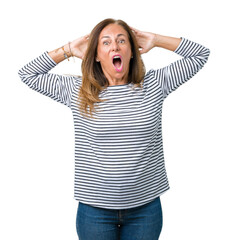 Obraz na płótnie Canvas Beautiful middle age woman wearing stripes sweater over isolated background Crazy and scared with hands on head, afraid and surprised of shock with open mouth