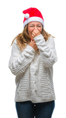 Middle age senior hispanic woman wearing christmas hat over isolated background smelling something stinky and disgusting, intolerable smell, holding breath with fingers on nose. Bad smells concept.