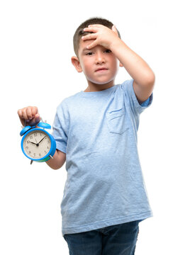 Little child holding alarm clock stressed with hand on head, shocked with shame and surprise face, angry and frustrated. Fear and upset for mistake.