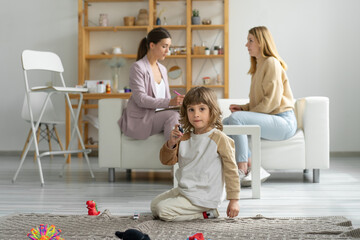 Mom and son at a consultation with a child psychologist. The boy plays with toys sitting on the floor. Family relationships.