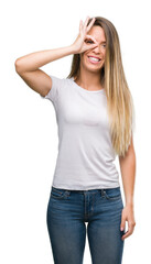 Fototapeta premium Beautiful young woman wearing t-shirt and jeans with happy face smiling doing ok sign with hand on eye looking through fingers