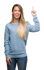 Beautiful young woman wearing sweater and jeans surprised with an idea or question pointing finger with happy face, number one