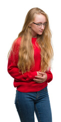 Blonde teenager woman wearing red sweater with hand on stomach because nausea, painful disease feeling unwell. Ache concept.