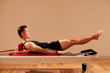 Fit man doing a lunge stretch yoga pilates exercise to strengthen and tone his muscles using a...