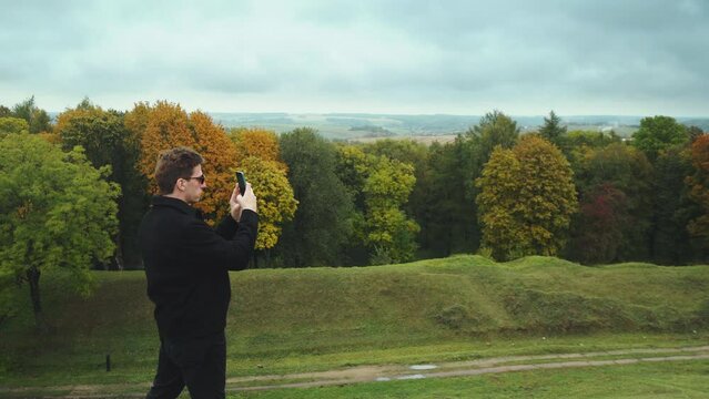 A guy in black clothes photographs the autumn landscape from a hill