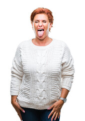 Atrractive senior caucasian redhead woman wearing winter sweater over isolated background sticking tongue out happy with funny expression. Emotion concept.