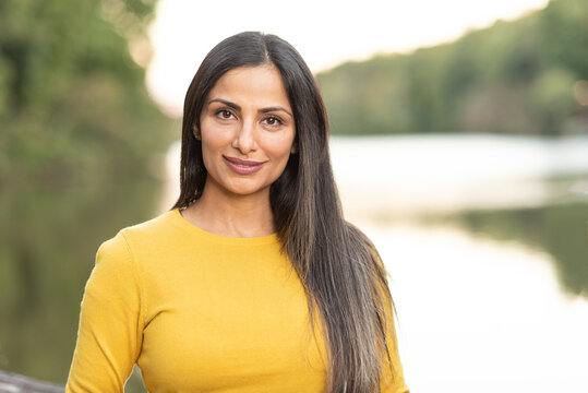 Beautiful Asian Indian woman in yellow sweater by a lake. 