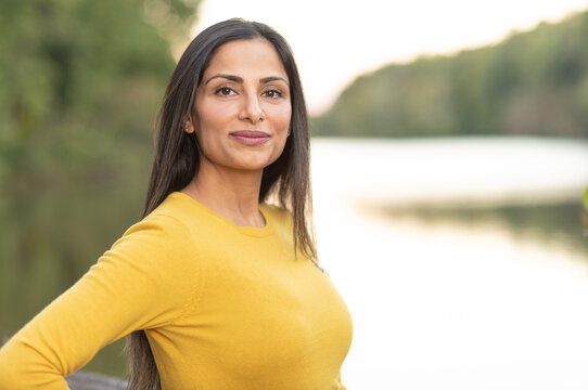 Beautiful Asian Indian woman in yellow sweater by a lake. 