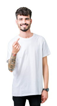 Young handsome man wearing white t-shirt over isolated background Beckoning come here gesture with hand inviting happy and smiling