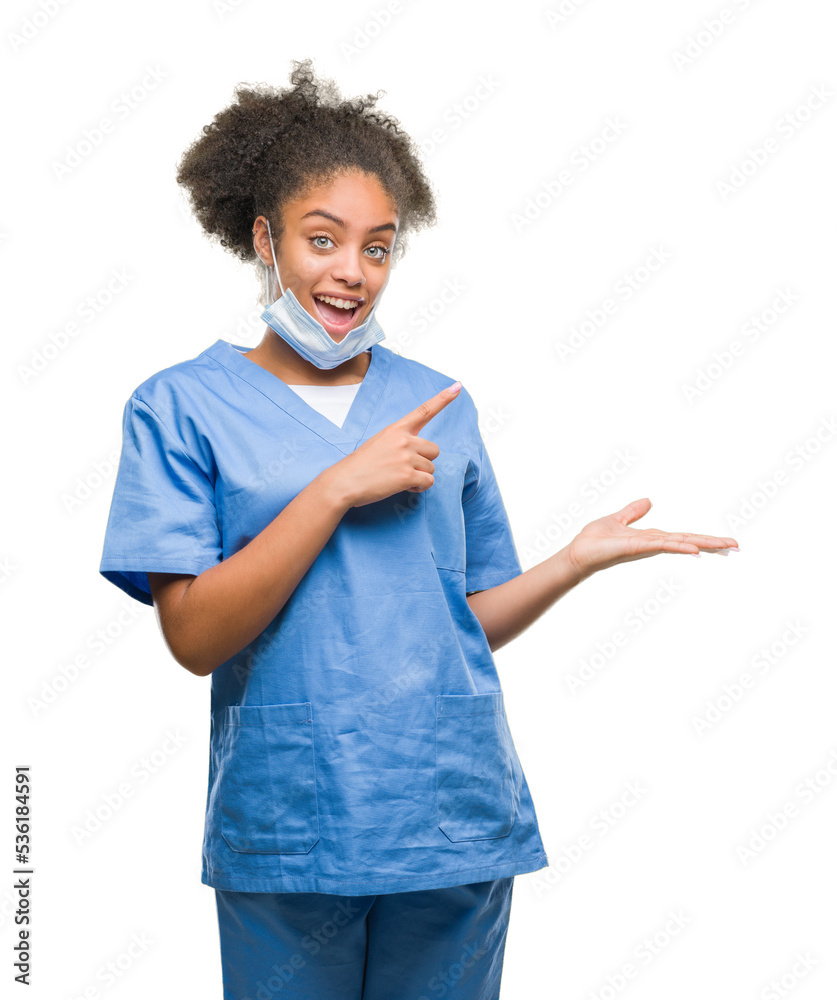 Poster Young afro american doctor woman over isolated background amazed and smiling to the camera while presenting with hand and pointing with finger.