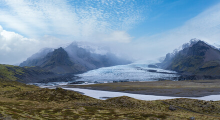 Glacier tongue slides from the Vatnajokull icecap or Vatna Glacier near subglacial Oraefajokull volcano, Iceland. Glacial lagoon with ice blocks and surrounding mountains.