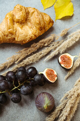 Autumn attributes. Croissant, dark grapes and figs on the grey table. Gold October