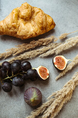 Autumn attributes. Croissant, dark grapes and figs on the grey table. Gold October