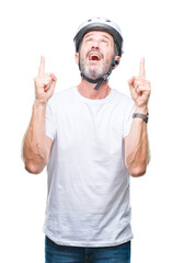 Naklejka premium Middle age senior hoary cyclist man wearing bike safety helment isolated background amazed and surprised looking up and pointing with fingers and raised arms.