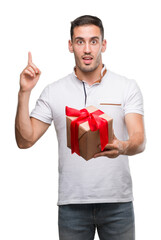 Handsome young man giving a present surprised with an idea or question pointing finger with happy face, number one