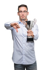 Handsome young man holding trophy with angry face, negative sign showing dislike with thumbs down,...