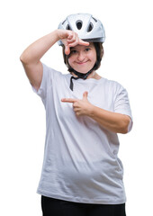 Young adult cyclist woman with down syndrome wearing safety helmet over isolated background smiling making frame with hands and fingers with happy face. Creativity and photography concept.